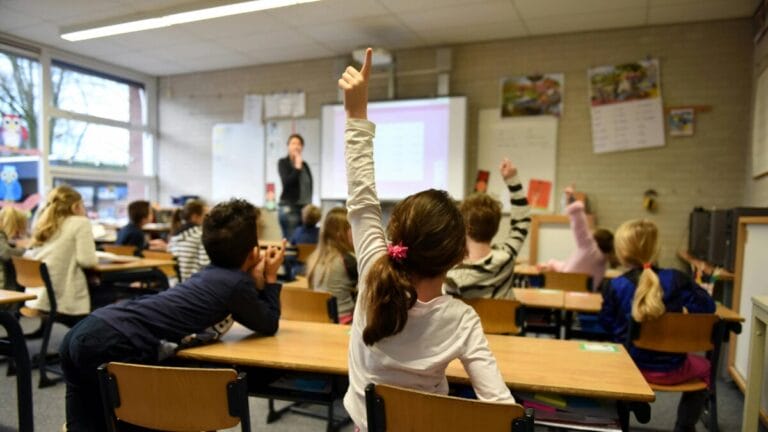 Een meisje in een basisschoolklas steekt haar hand op